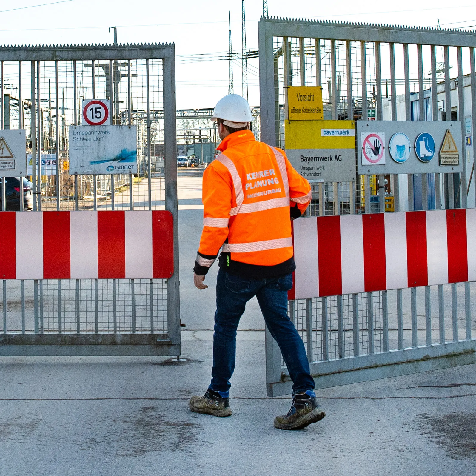 Mitarbeiter in Warnjacke und Helm von hinten auf Betriebsgelände