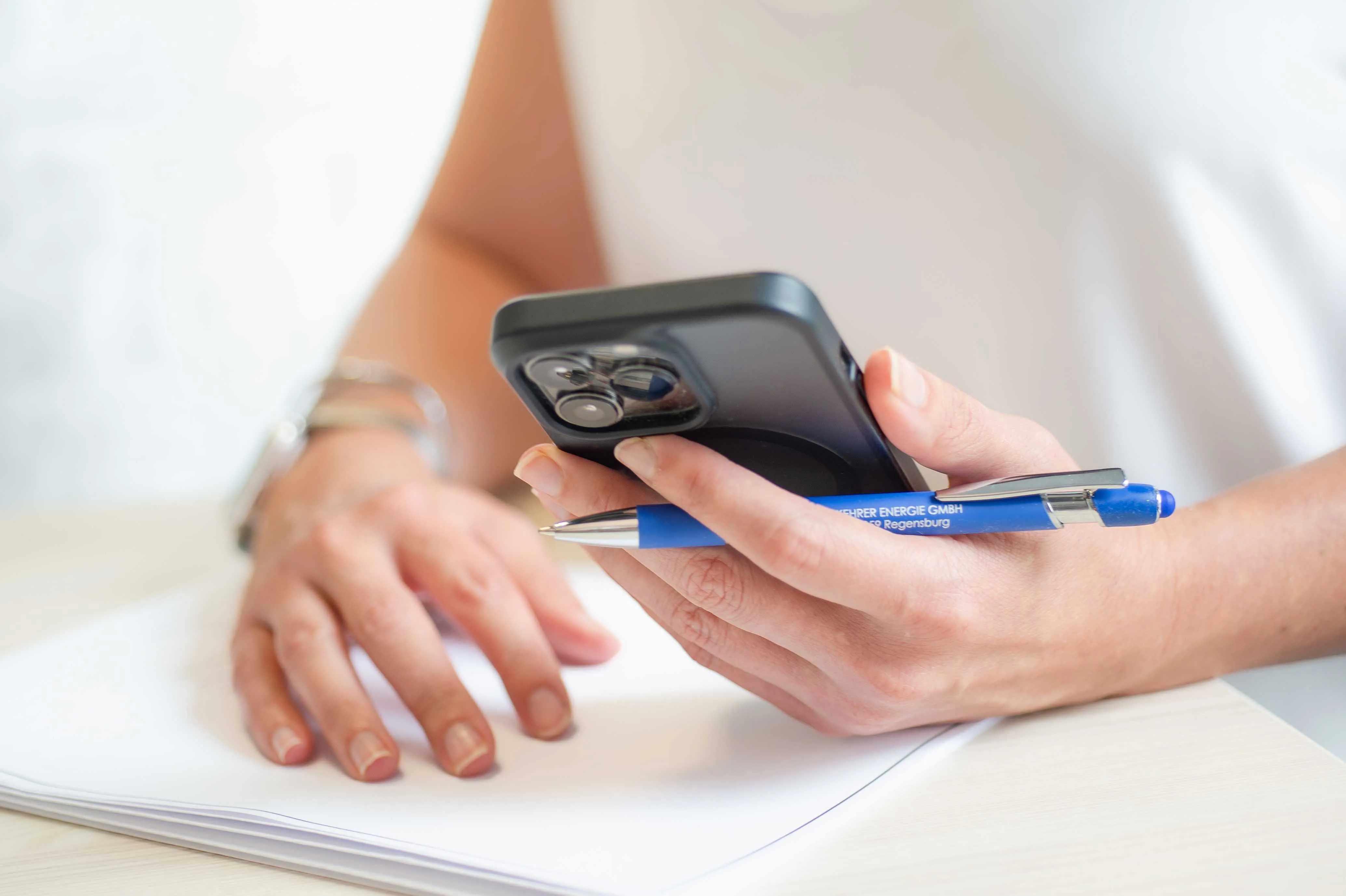 Person mit Hand auf Papier liegend. Handy und Stift der anderen Hand haltend